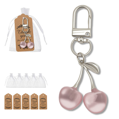 A pink double cherry keychain shown beside a white drawstring pouch and printed thank-you tags.