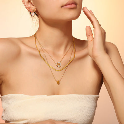 Model wearing layered gold necklaces with heart and oval bead