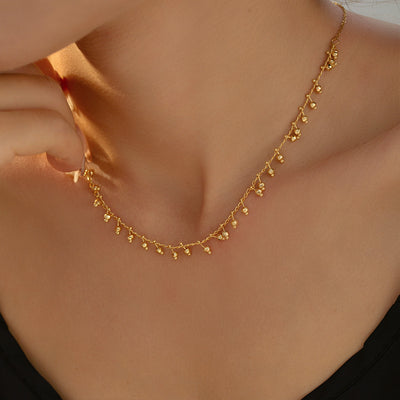 Woman wearing gold mini ball drop pendant necklace on bare collarbone