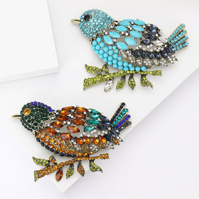 Grouped view of oversized perched bird brooch densely covered in crystals arranged together.