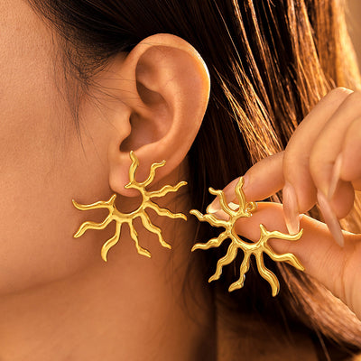 Gold sunburst open stud worn while holding matching earring