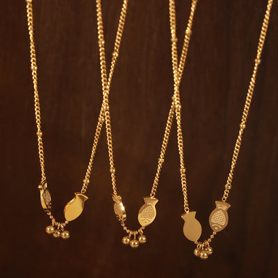 Three gold double fish charm necklaces hanging on dark wood
