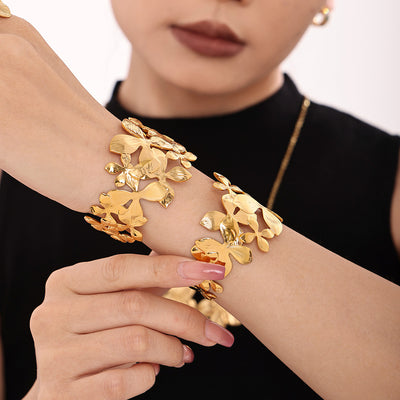 Model wrists stacked with gold openwork floral cuff bracelets