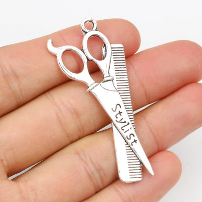 Hand held view of the scissors and comb hairdresser pendant showing the front shape and finish