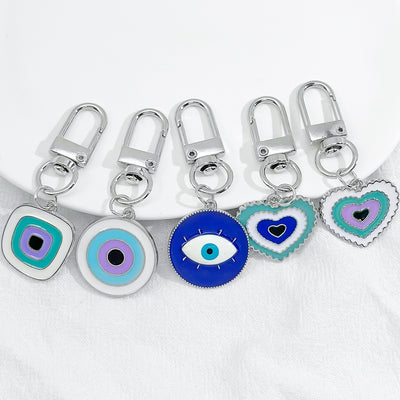 Five evil eye enamel keychains in blue, purple and teal displayed on white cloth