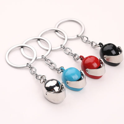 Four motorcycle helmet keychains in silver, blue, red, and black arranged on a pale background.