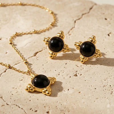 Gold black cabochon pendant and matching stud earrings on stone surface