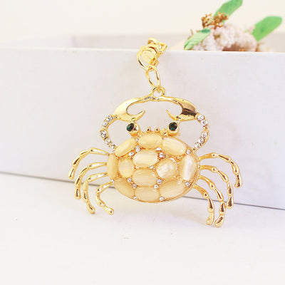 Front view of a gold-tone crab charm with cream oval inlays and clear stones.