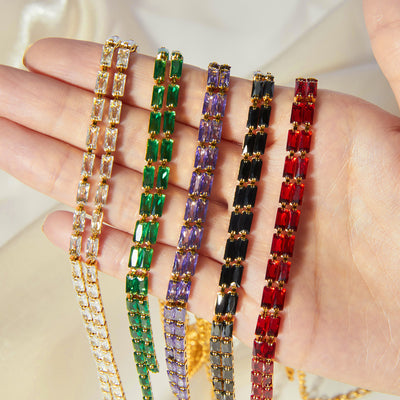 Hand holding five gold rectangular-stone Y necklaces white green purple black red