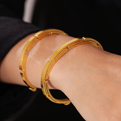 Two gold geometric open cuff bangles stacked on wrist in close-up