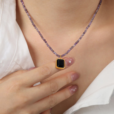 Purple bead necklace with black gold-framed pendant worn at neckline