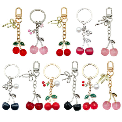 Clean white background catalog view of nineteen cherry keychains with varied clasps and initial tags