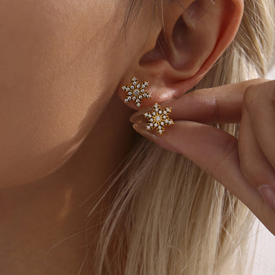 Clear zircon gold snowflake studs, one worn and one held by fingers