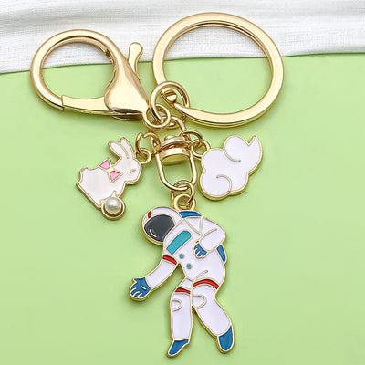 Close-up of a gold-tone astronaut keychain with white rabbit and cloud charms.
