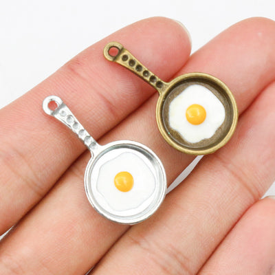 Fried Egg Frying Pan Enamel Charms in Two Antique Finishes assortment on a plain background