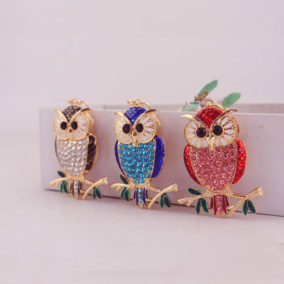 Three black, blue, and red rhinestone owls rest against a white box.