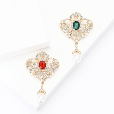 Front view of an ornate crown-like brooch with a colored center stone and pearl drop