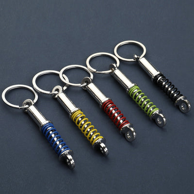 Five shock absorber keychains with blue, yellow, red, green, and black coil springs.