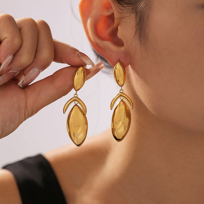 Model holding gold geometric leaf drop earrings near ear