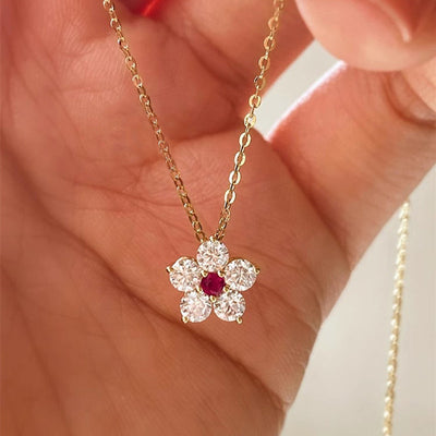 Gold flower pendant necklace with red center held in hand