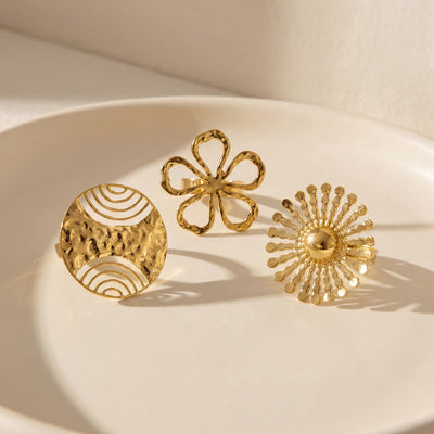 Three gold open rings sunburst flower and wave disc on white plate