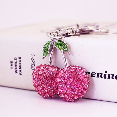 Close-up of two pink rhinestone cherries with green leaves and key ring hardware