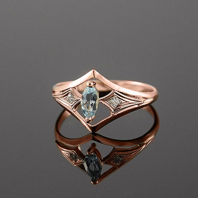 Rose gold diamond V ring with marquise light blue stone on dark reflective surface