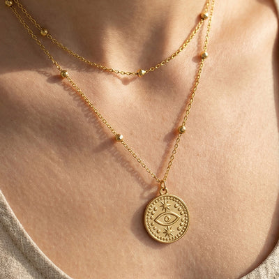 Gold double-layer evil eye coin necklace worn at collarbone close-up