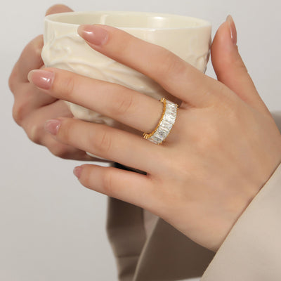Model wearing gold baguette eternity ring while holding white cup