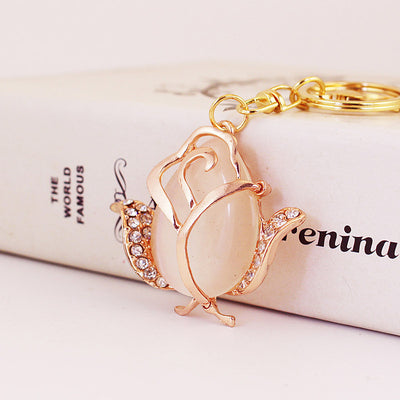 Front view of a cream rose charm with clear stones beside a gold-tone split key ring.