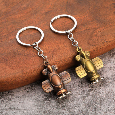 Antique copper and antique bronze airplane keychains displayed on wood and gray fabric.
