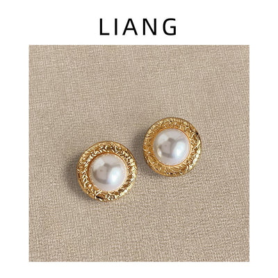 Gold textured round pearl studs on beige linen under brand frame