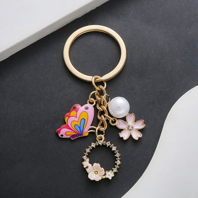 Front product photo of pink butterfly pearl and open flower enamel charm keychain showing the pictured design arrangemen