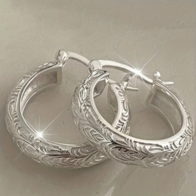 Silver floral engraved thick huggie hoops stacked on pale surface
