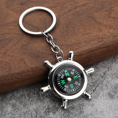 Close-up of a silver-tone ship wheel compass keychain on wood and gray fabric