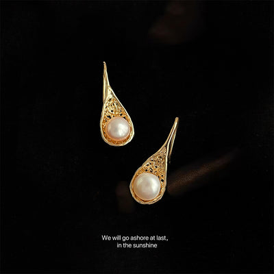 Pair of gold teardrop filigree pearl hooks on black velvet