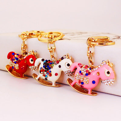 Red, white, and pink rocking horse keychains with multicolor stones are shown together.