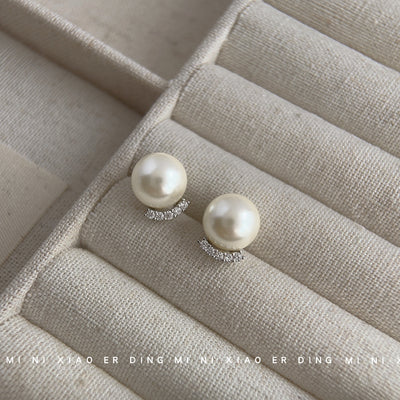 Cream pearl studs with silver crescent pavé on beige jewelry tray