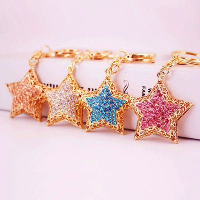 Four gold tone star keychains display peach, clear, blue, and pink rhinestone centers.