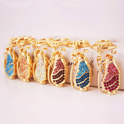 A row of gold-tone golf bag keychains set with blue, pink, clear, and purple rhinestones.