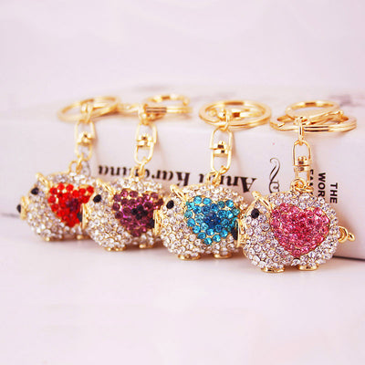 Four gold-tone pig keychains with red, purple, blue, and pink rhinestone hearts.