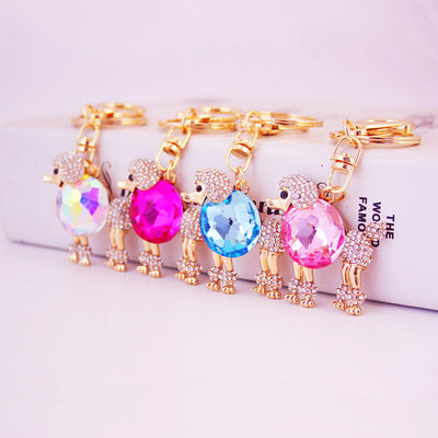 Four gold-tone poodle keychains displayed with iridescent, magenta, blue, and pink faceted centers.