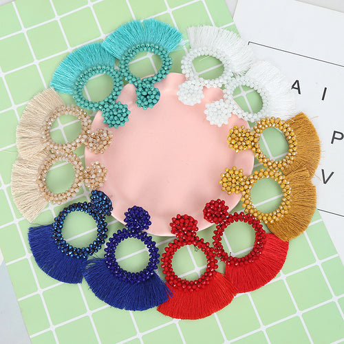 Six colors of crystal bead flower hoop fringe earrings arranged in a circle on a green tile background