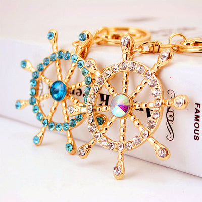 Two gold-tone ship wheel keychains with clear and blue rhinestones.