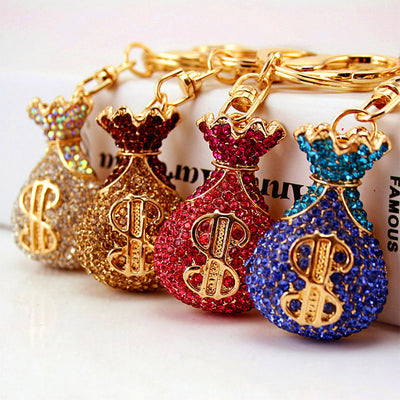 Four rhinestone money bag keychains in white, gold, red, and blue are arranged together.