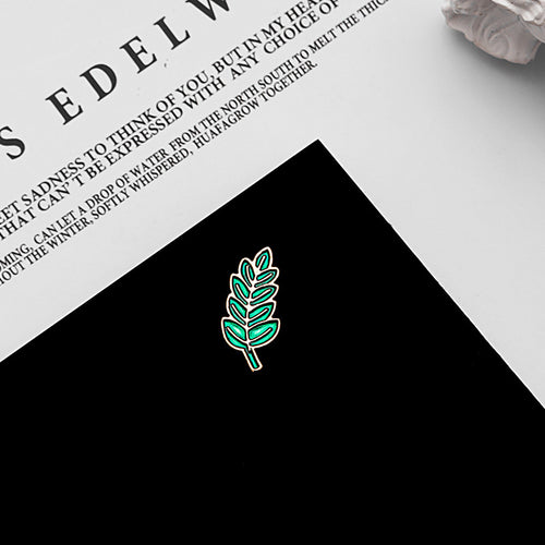 Green enamel leaf brooch on black surface beside printed book page