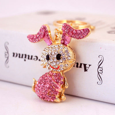 Close-up of a pink rhinestone rabbit charm in front of a gold-tone key ring.