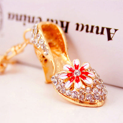 Close view of a gold-tone high heel keychain with a red-and-white daisy and clear rhinestones.