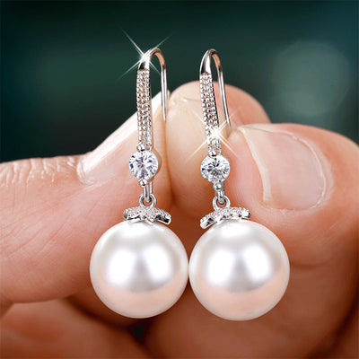 White pearl drop hook earrings held between fingers close-up