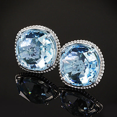 Pair of light blue cushion CZ studs with silver beaded rims on black reflective surface